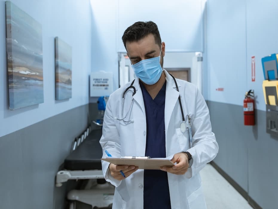 Healthcare provider wearing a mask uses a digital tablet for cloud-based communications to enable continuity of care.