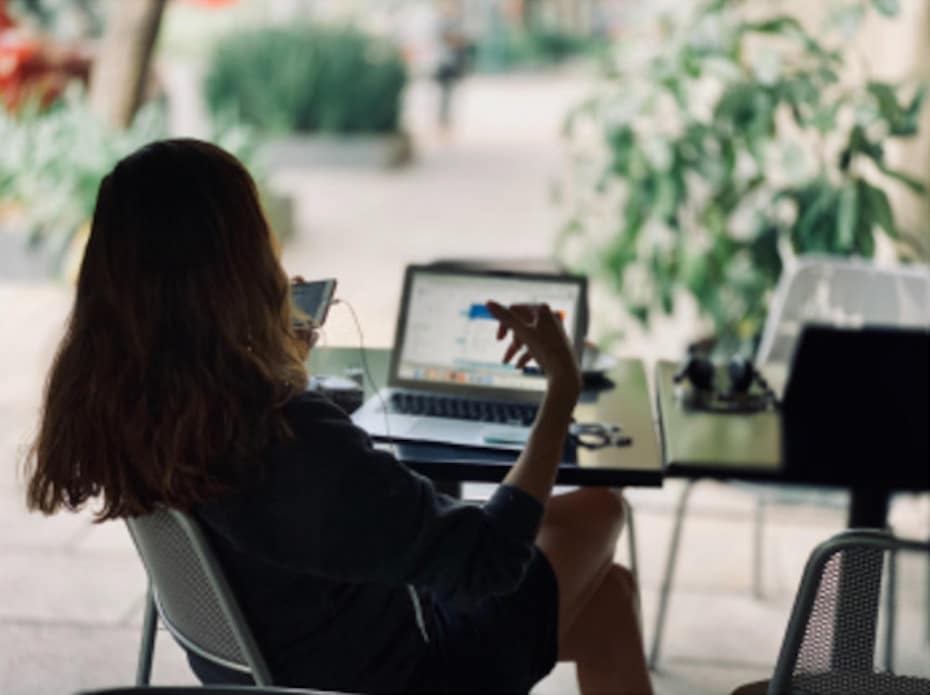 A woman sitting in a tropical setting talking on a mobile phone and using a laptop to depict work-life balance for insurance employees.
