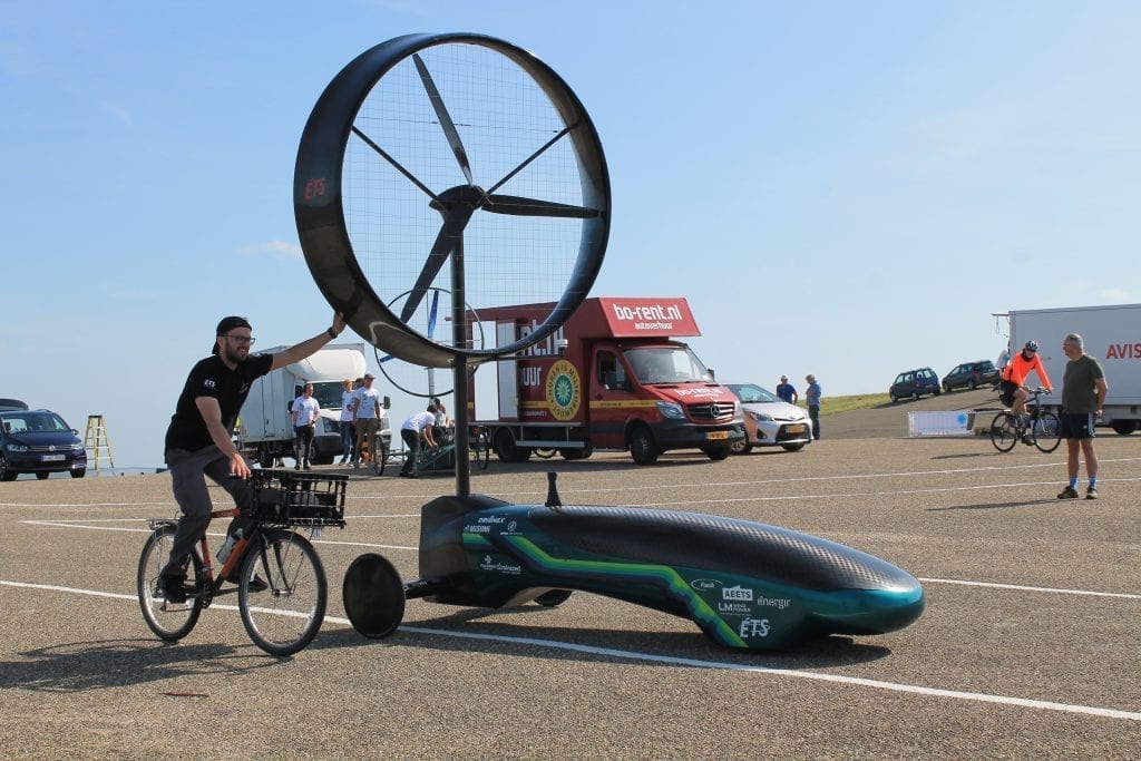 A chinook team member on a bike seen holding the propeller of a Chinook car.