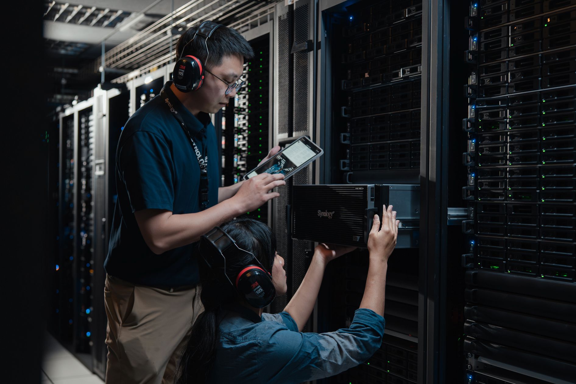 Synology QA team members examining and loading a PAS series system into a row of rackmount systems in a datacenter.